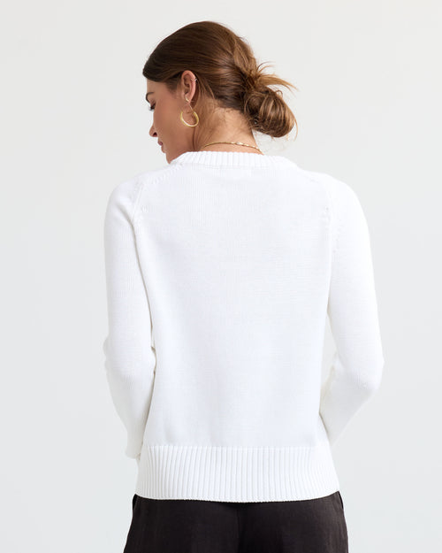 LIFESTYLE / EDITORIAL: Woman wearing cream cashmere sweater, back view, hair in bun, gold hoop earrings, white background