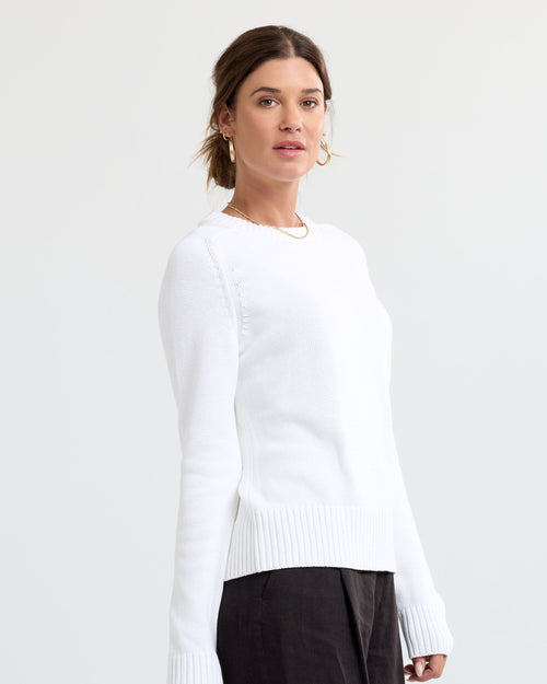 LIFESTYLE / EDITORIAL: Woman wearing a cream cashmere sweater with long sleeves and ribbed cuffs, standing against a white