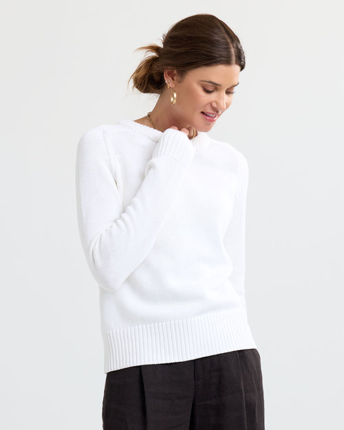 LIFESTYLE / EDITORIAL: Woman wearing cream cashmere sweater and dark pants, looking down with hair in a low bun
