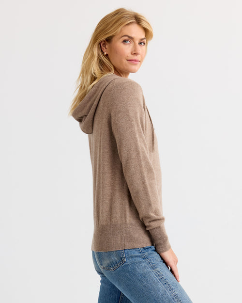 LIFESTYLE / EDITORIAL: Woman in driftwood-colored cashmere hoodie and blue jeans, side view against white background