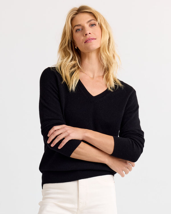 LIFESTYLE / EDITORIAL: Woman wearing black V-neck cashmere sweater and white pants, standing with arms crossed against white