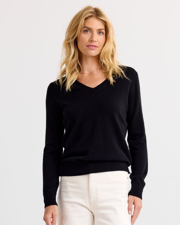 Front view image of a woman wearing a black V-neck cashmere sweater and white pants against a plain background