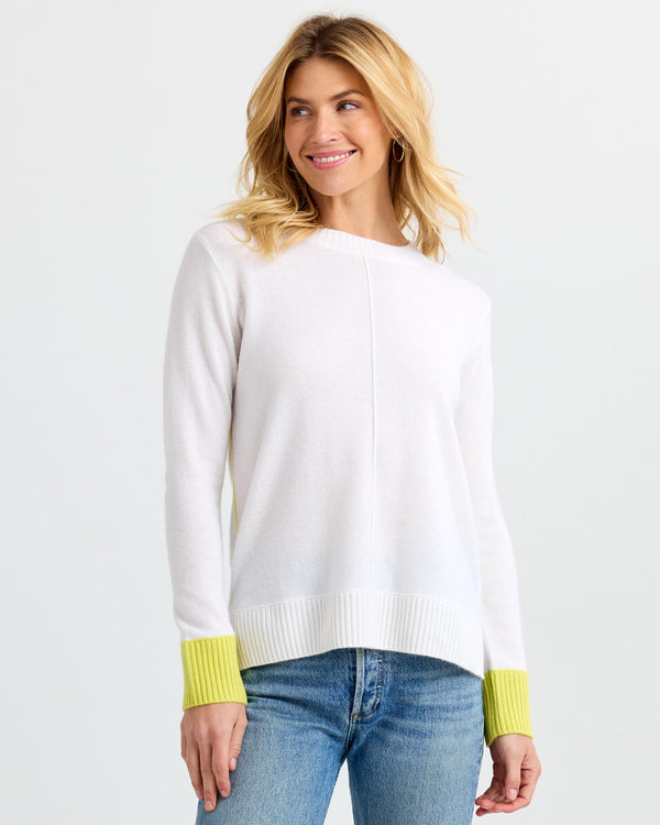 Three-quarter view image of a woman wearing a white cashmere sweater with yellow cuffs and blue jeans smiling