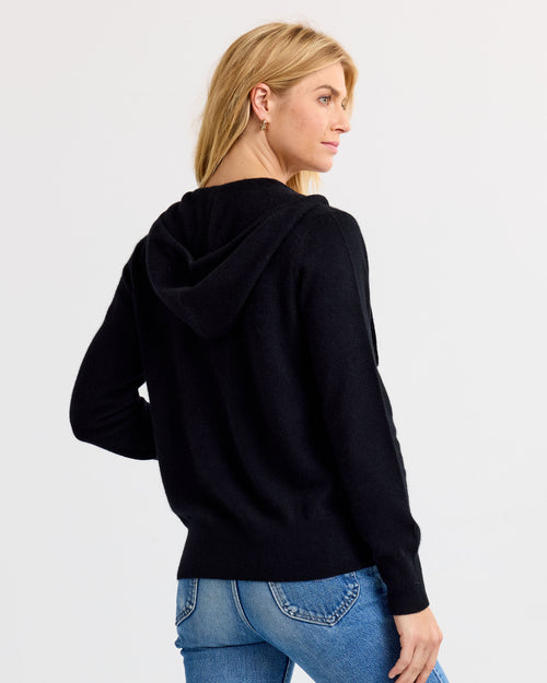 LIFESTYLE / EDITORIAL: Woman wearing black cashmere hoodie and blue jeans, viewed from back against white background