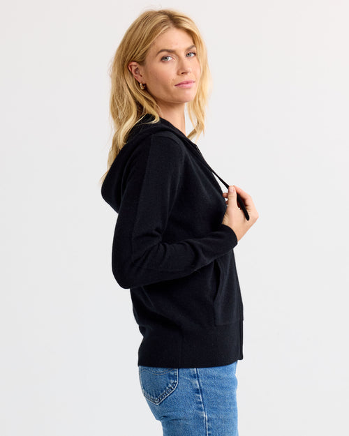 LIFESTYLE / EDITORIAL: Woman in black cashmere hoodie and blue jeans, side view, neutral background
