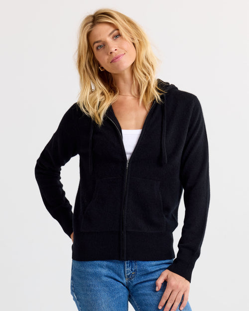 Front view image of a woman wearing a black zip-up cashmere hoodie with blue jeans against a white background