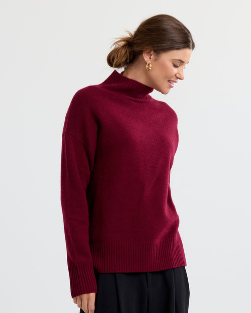 LIFESTYLE / EDITORIAL: Woman wearing a barolo red cashmere turtleneck sweater with black pants, side profile pose