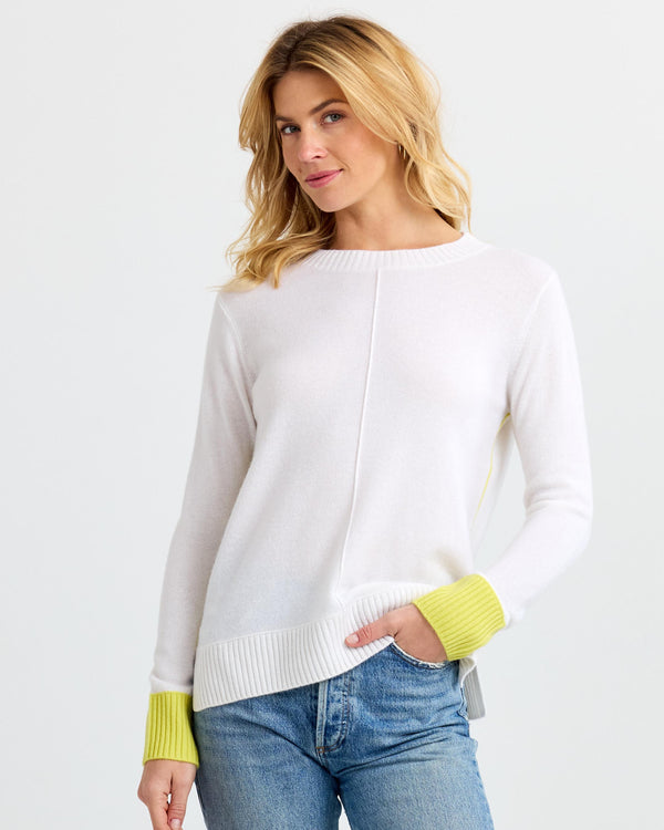 LIFESTYLE / EDITORIAL: Woman wearing white cashmere sweater with yellow cuffs and blue jeans against white background