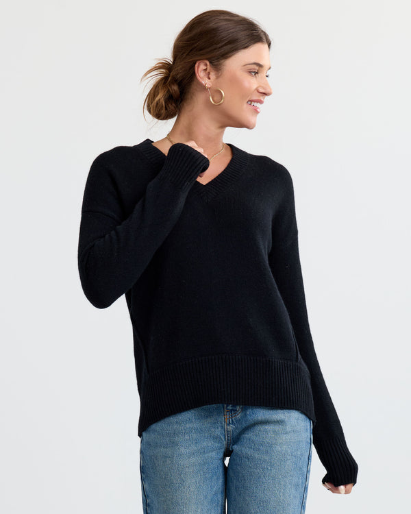 LIFESTYLE / EDITORIAL: Woman wearing black V-neck cashmere sweater and blue jeans, smiling and looking to side