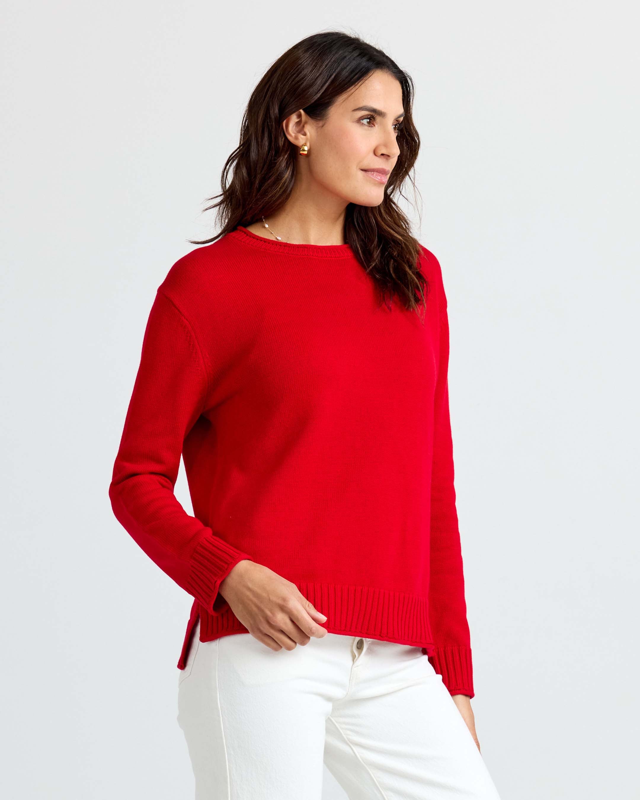 LIFESTYLE / EDITORIAL: Woman wearing red cashmere sweater and white pants, standing against a plain light background