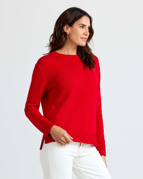 LIFESTYLE / EDITORIAL: Woman wearing red cashmere sweater and white pants, standing against a plain light background
