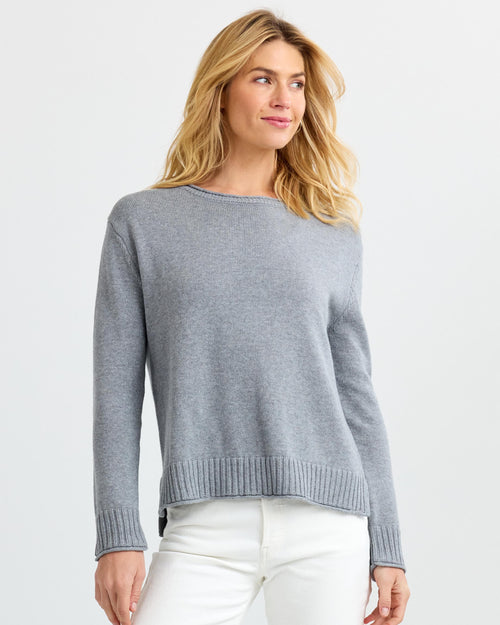 LIFESTYLE / EDITORIAL: Woman wearing light gray cashmere sweater and white pants against plain background