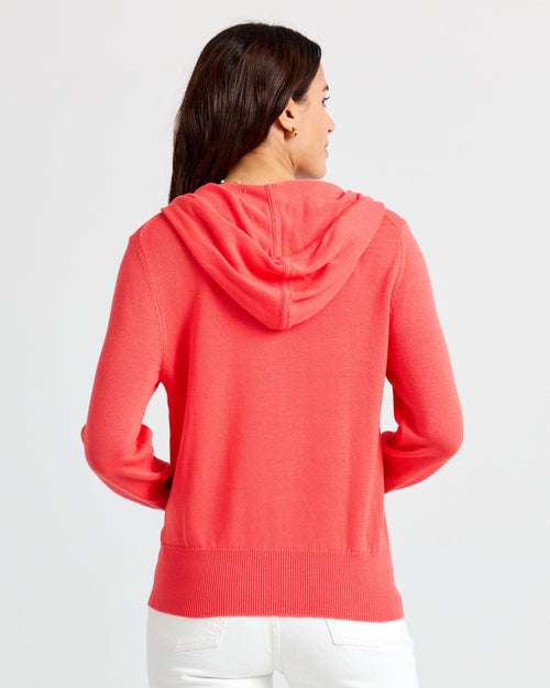 LIFESTYLE / EDITORIAL: Woman wearing coral cashmere hoodie, shown from back, with white pants against plain background