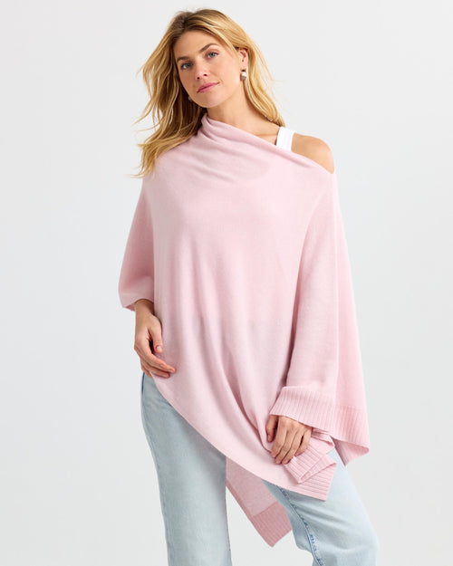 LIFESTYLE / EDITORIAL: Woman wearing blush pink cashmere poncho over white top and light blue jeans against white background