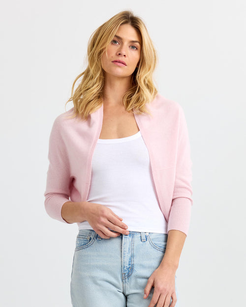 LIFESTYLE / EDITORIAL: Woman wearing light pink cashmere shrug over white tank top and light blue jeans against white
