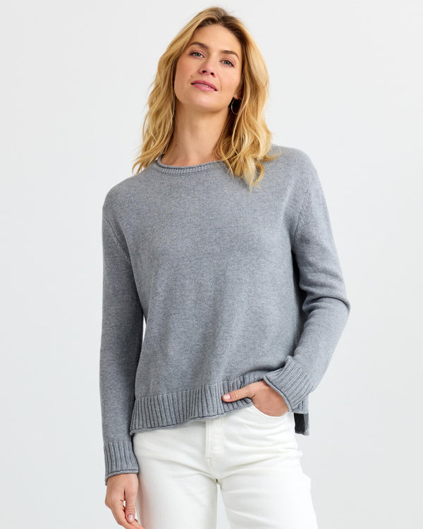LIFESTYLE / EDITORIAL: Woman wearing grey cashmere sweater and white pants against plain white background