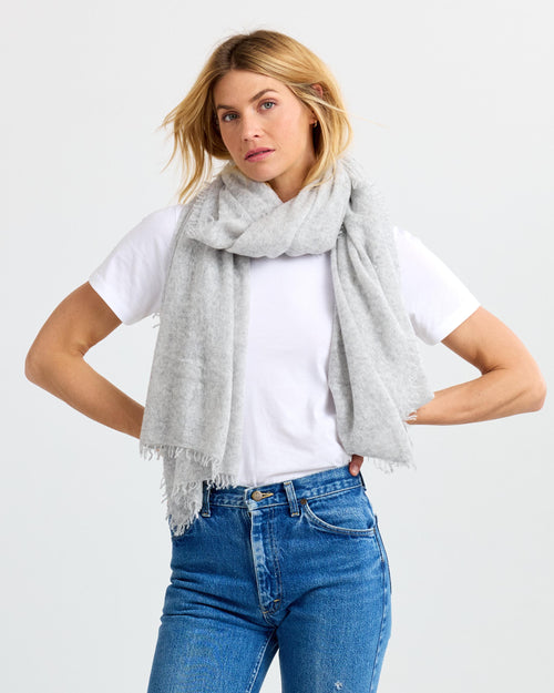 Front view image of a woman wearing a light gray cashmere scarf draped over a white t-shirt and blue jeans