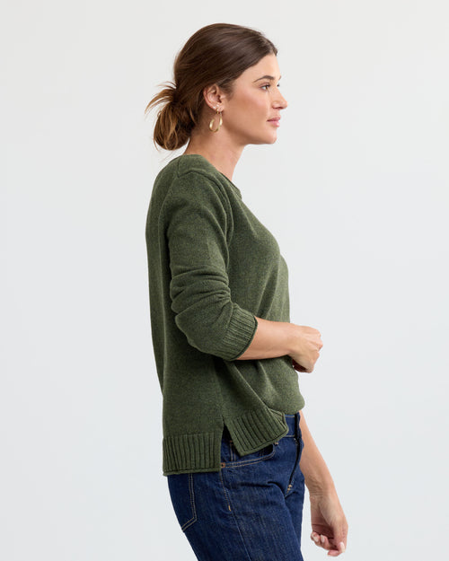 LIFESTYLE / EDITORIAL: Woman in profile wearing green cashmere sweater and blue jeans against a plain background