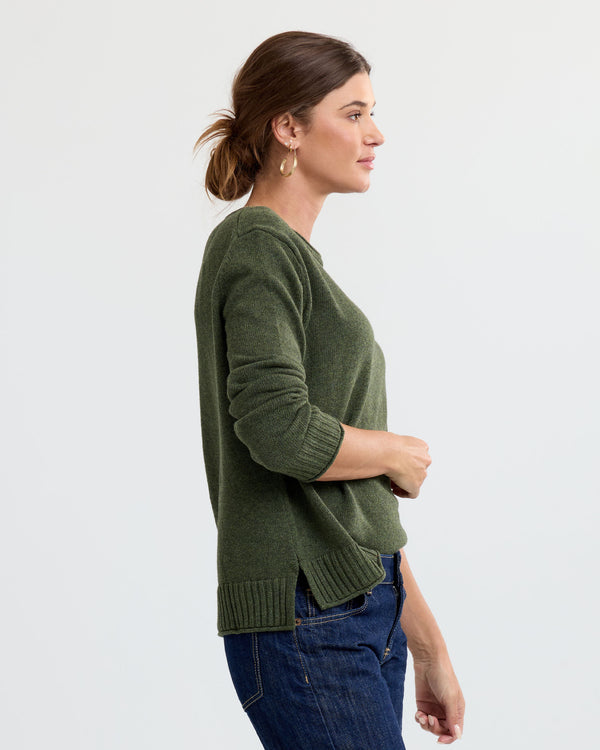 LIFESTYLE / EDITORIAL: Woman in profile wearing green cashmere sweater and blue jeans against a plain background