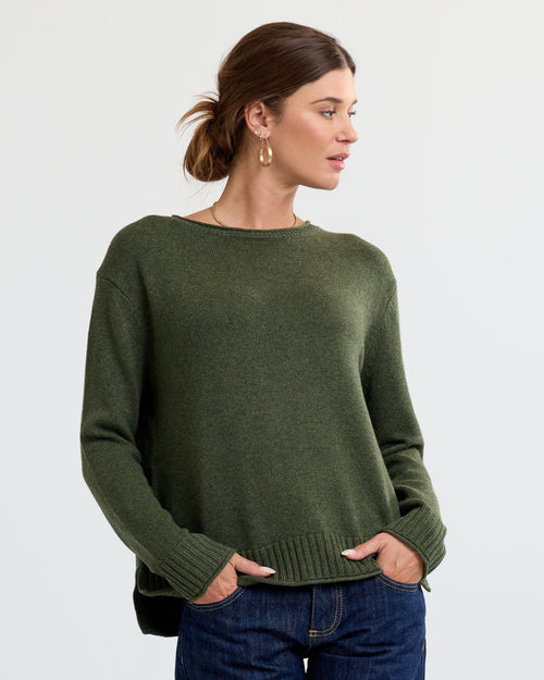 LIFESTYLE / EDITORIAL: Woman wearing olive green cashmere sweater and jeans, standing against plain background