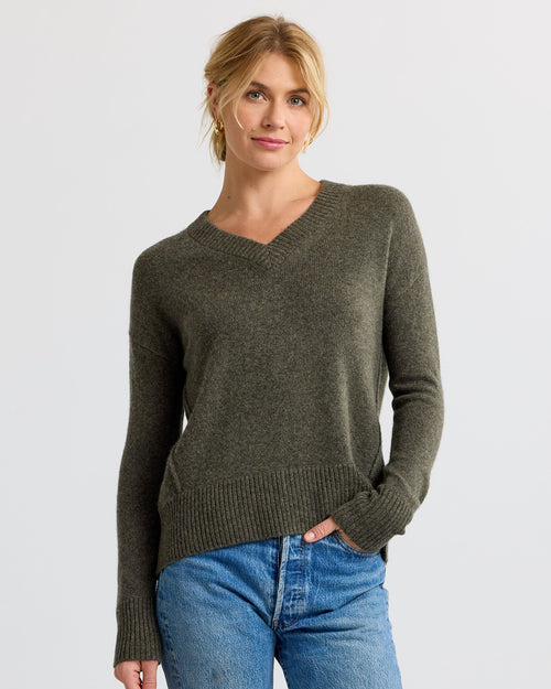 Front view image of a woman wearing an olive green V-neck cashmere sweater and blue jeans with hand in pocket