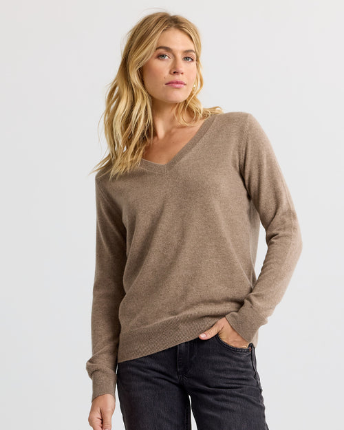 Three-quarter view image of a woman wearing a driftwood brown V-neck cashmere sweater and black jeans.