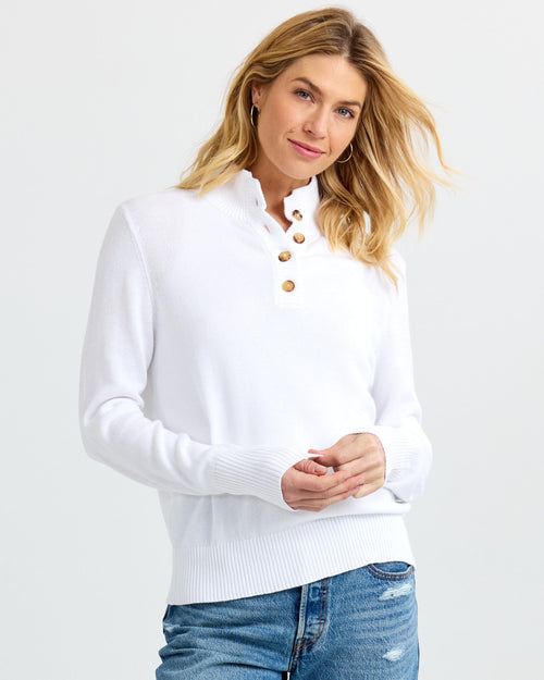 LIFESTYLE / EDITORIAL: Woman wearing white buttoned cashmere sweater and blue jeans against plain background