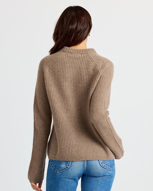 Woman wearing driftwood-colored ribbed cashmere sweater and blue jeans, shown from the back against white background