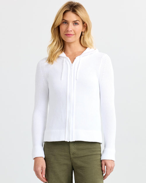 LIFESTYLE / EDITORIAL: Woman wearing white zip-up ribbed cashmere hoodie and olive pants against plain background