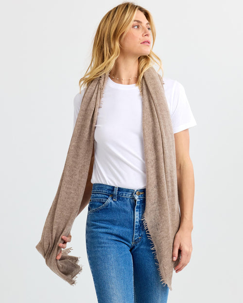 LIFESTYLE / EDITORIAL: Woman wearing beige cashmere scarf over white t-shirt and blue jeans, looking to the side