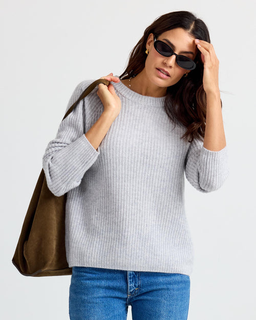 LIFESTYLE / EDITORIAL: Woman wearing gray ribbed cashmere sweater, blue jeans, sunglasses, carrying brown suede bag