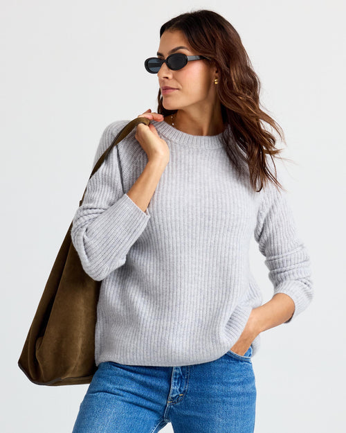 LIFESTYLE / EDITORIAL: Woman wearing gray ribbed cashmere sweater, blue jeans, sunglasses, and carrying large brown suede bag