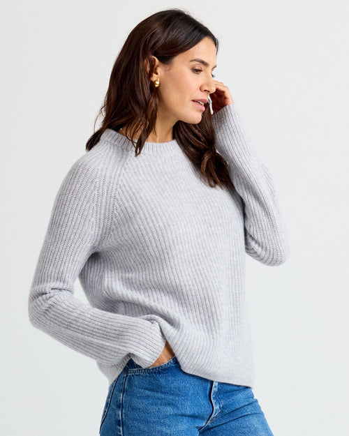 LIFESTYLE / EDITORIAL: Woman wearing light gray ribbed cashmere sweater and blue jeans, side profile against white background