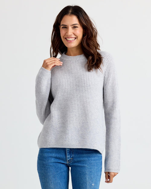 LIFESTYLE / EDITORIAL: Woman smiling wearing light gray ribbed cashmere sweater and blue jeans against white background