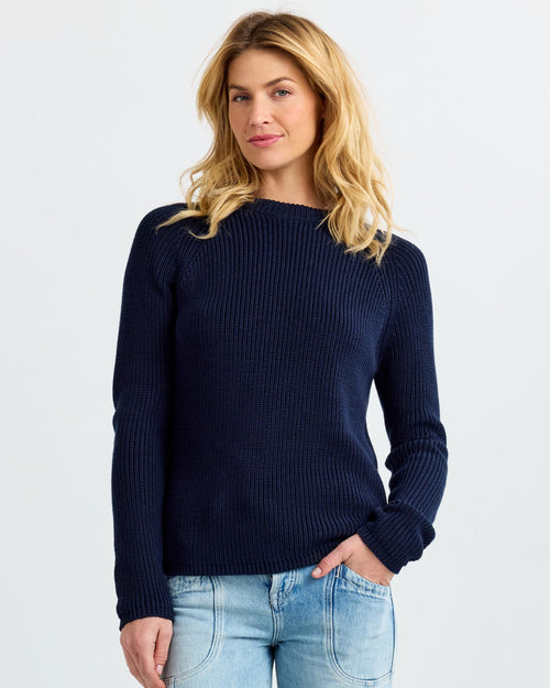 Woman wearing navy ribbed cashmere sweater and light blue jeans, standing against white background