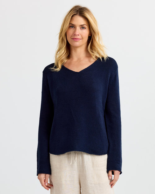 LIFESTYLE / EDITORIAL: Woman wearing navy V-neck cashmere sweater and light beige pants against white background