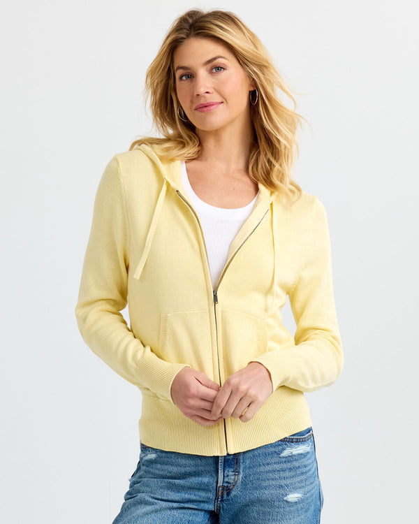 LIFESTYLE / EDITORIAL: Woman wearing a buttermilk yellow zip-up cashmere hoodie over white top and blue jeans