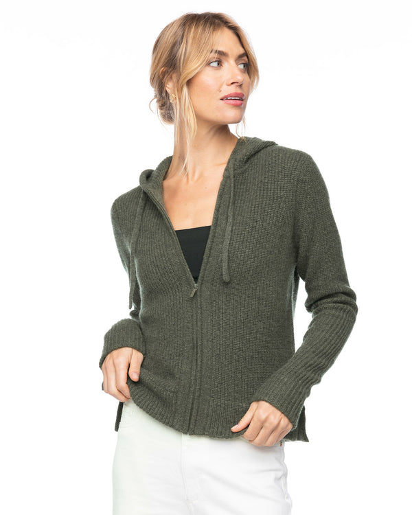 LIFESTYLE / EDITORIAL: Woman wearing dark olive cashmere zip-up hoodie with hood, paired with white pants, looking sideways