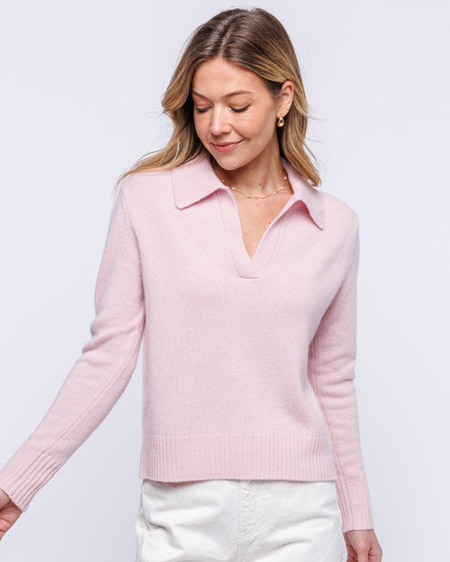 Woman wearing blush pink cashmere polo crew sweater with collar and white pants against light background
