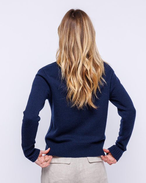 Woman with long blonde hair wearing navy blue cashmere crewneck sweater, back view, beige pants visible