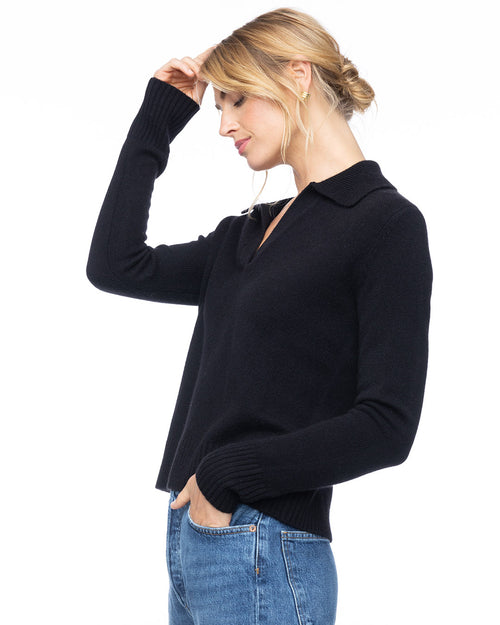 Woman wearing black cashmere polo V-neck sweater with collar and blue jeans, side view against white background
