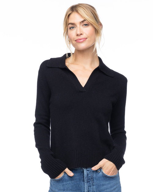 Woman wearing black cashmere polo V-neck sweater with collar and blue jeans, hands in pockets, white background
