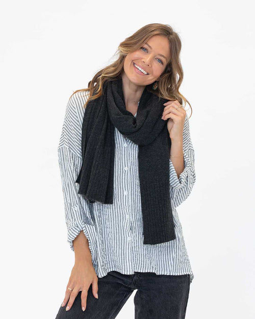 LIFESTYLE / EDITORIAL: Smiling woman wearing charcoal cashmere travel wrap scarf and striped shirt against white background