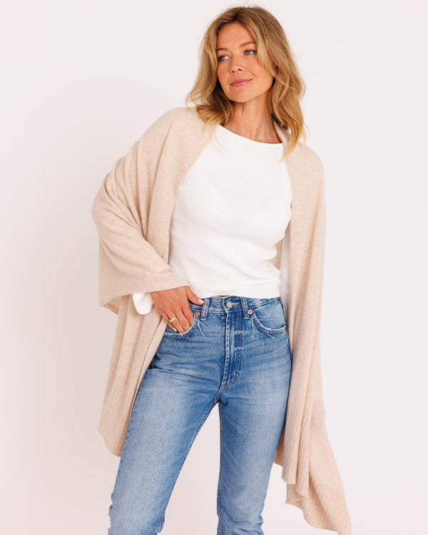LIFESTYLE / EDITORIAL: Woman wearing oatmeal cashmere wrap over white top and blue jeans against plain background