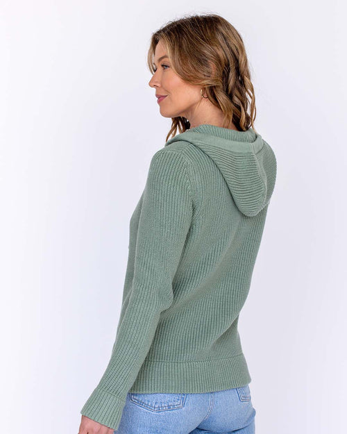 LIFESTYLE / EDITORIAL: Woman wearing sage green ribbed cotton hoodie, viewed from back and side, with light blue jeans