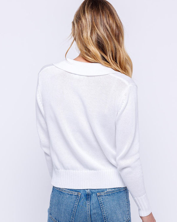 LIFESTYLE / EDITORIAL: Woman wearing white cotton polo V-neck sweater, shown from back, paired with blue jeans