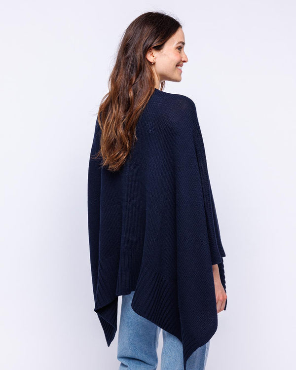 LIFESTYLE / EDITORIAL: Woman wearing navy cotton serape, shown from back, paired with light blue jeans against white