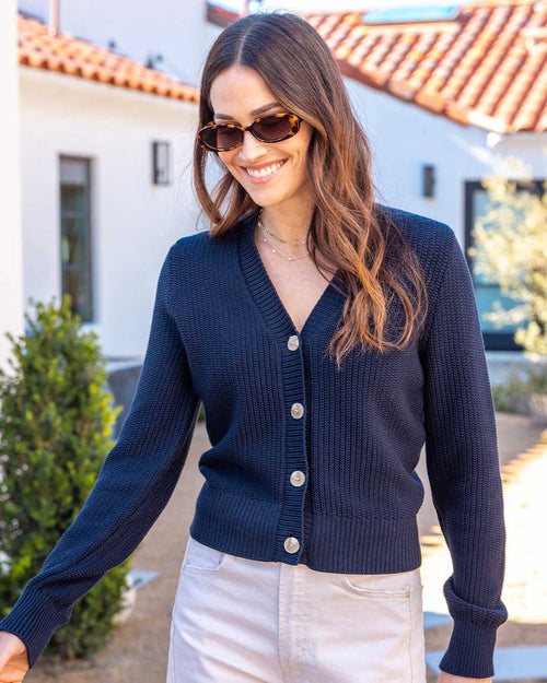 LIFESTYLE / EDITORIAL: Woman wearing navy textured cotton cardigan and sunglasses outdoors near white building with red roof