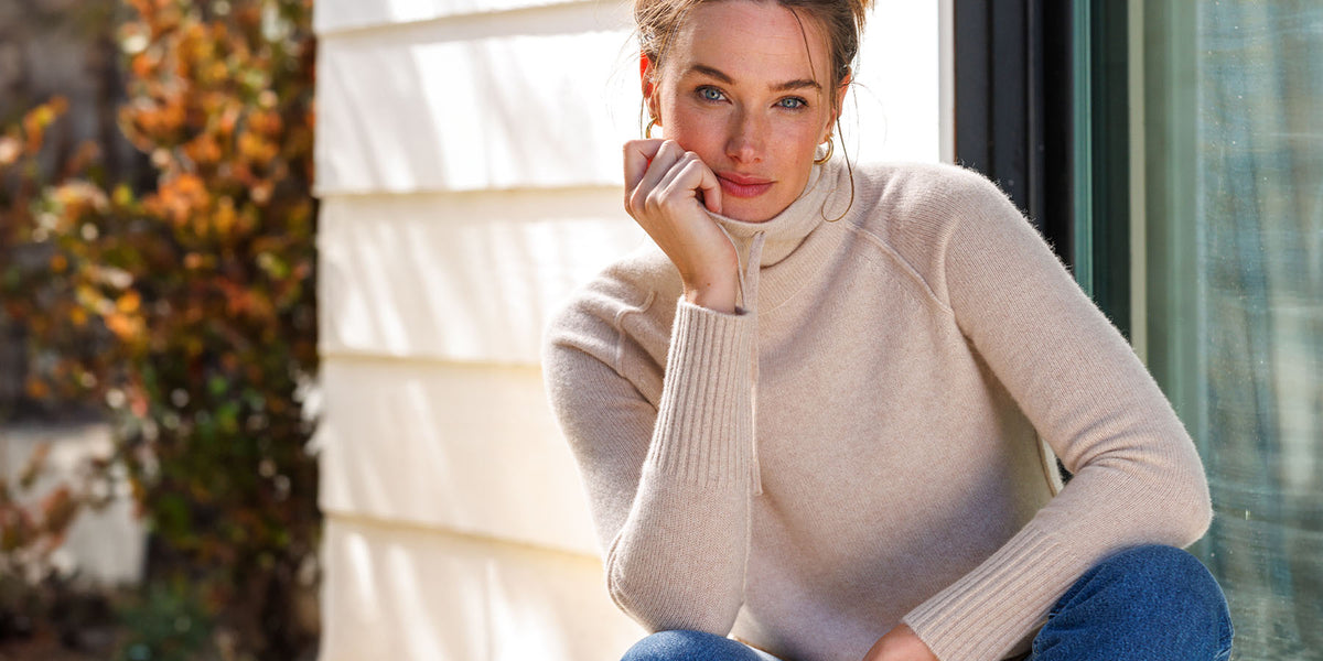 LIFESTYLE / EDITORIAL: Woman in beige cashmere sweater sitting by window with autumn foliage outside