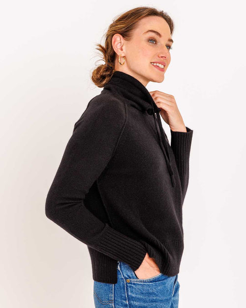 LIFESTYLE / EDITORIAL: Woman wearing black drawstring funnel neck cashmere sweater with blue jeans, side profile pose